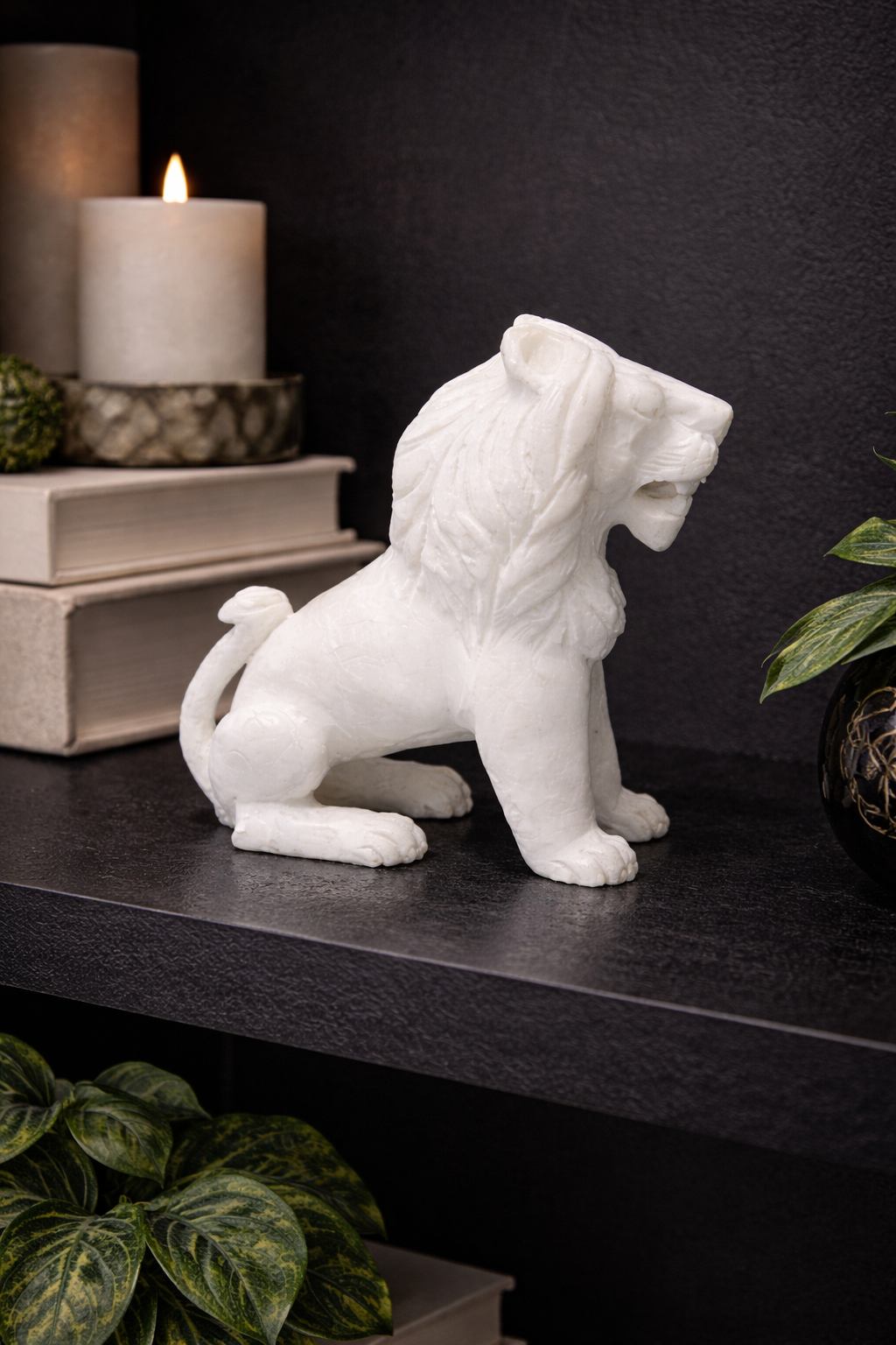 Polished white marble sitting lion sculpture on dark shelf with candle and indoor plants