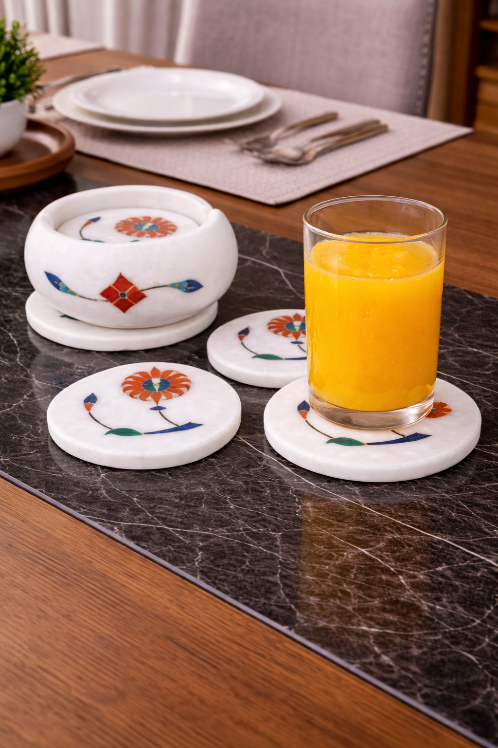 Luxury white marble coaster set with floral pietra dura inlay holding a glass of orange juice on a coffee table