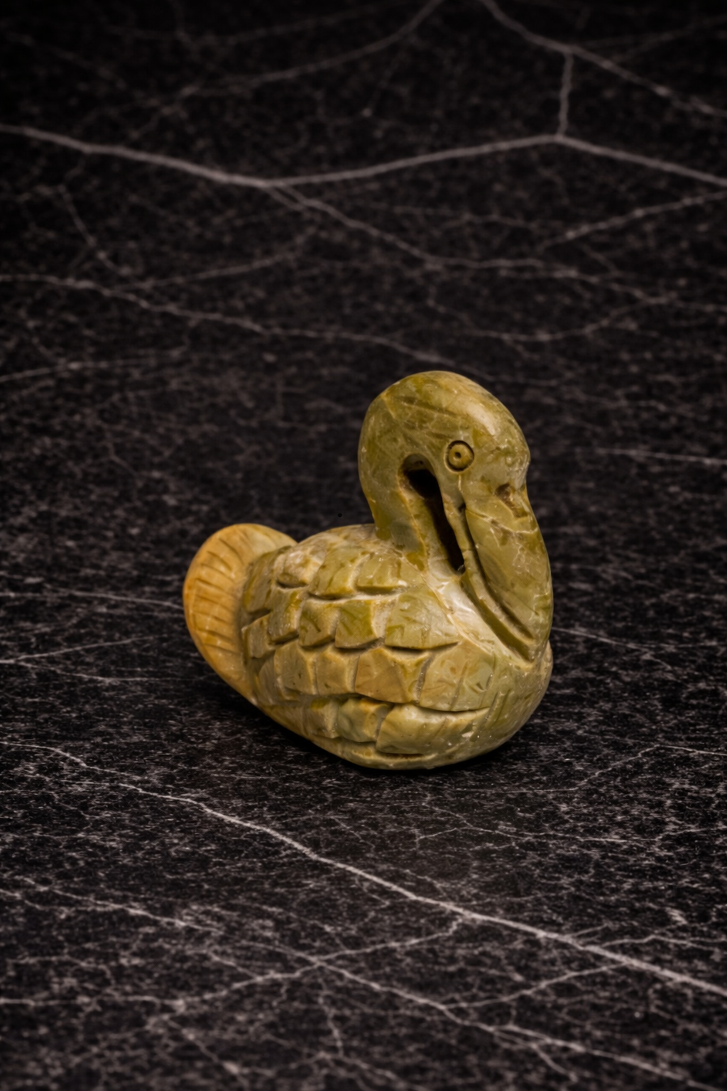 Small, polished soapstone duck sculpture in natural stone tones displayed on dark marble surface