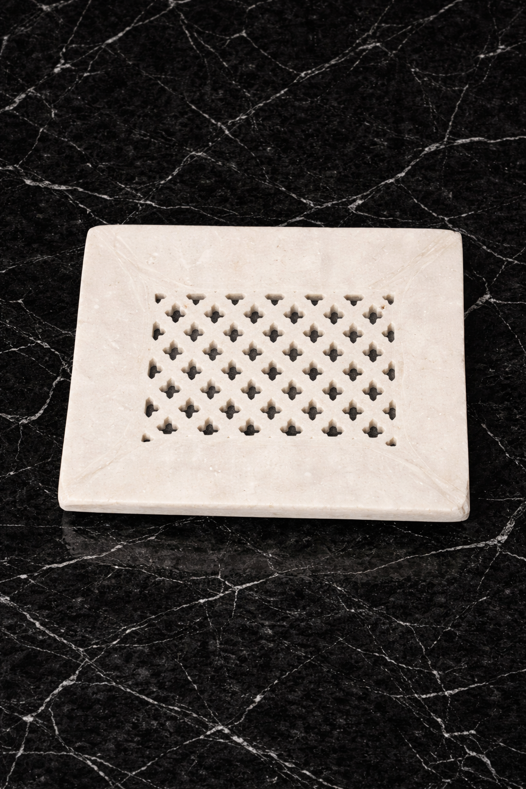 White marble tray with intricate cut-out pattern on a black textured background