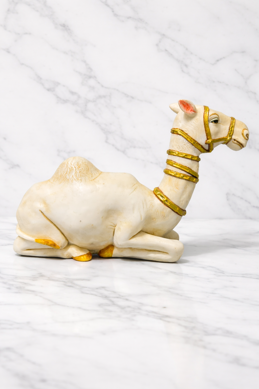 Handmade white camel décor figurine with gold accents on white marble surface
