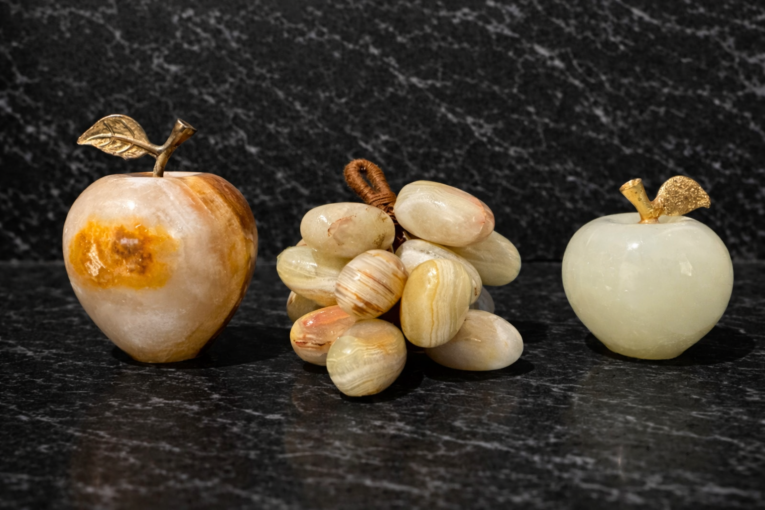 Onyx apple and grape decor set on a dark marble surface