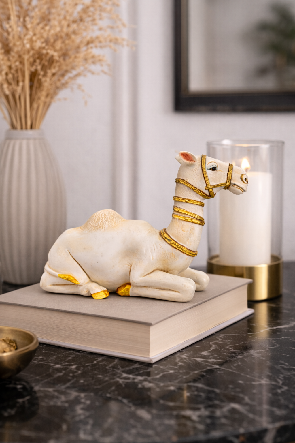 White camel figurine with gold accents on a book beside a candle