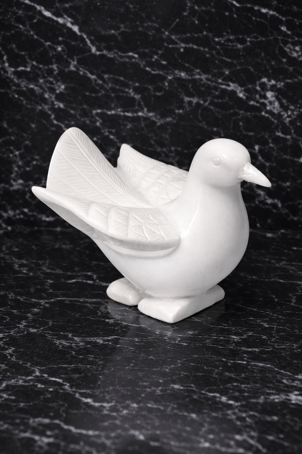 Hand-carved white marble dove statue on black marble surface