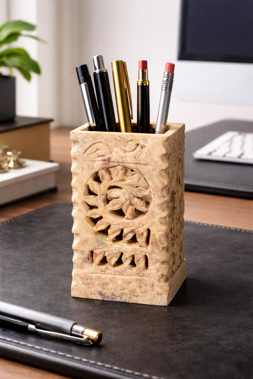 Hand-carved square soapstone pen holder with floral cut-out design, holding pens on a desk workspace