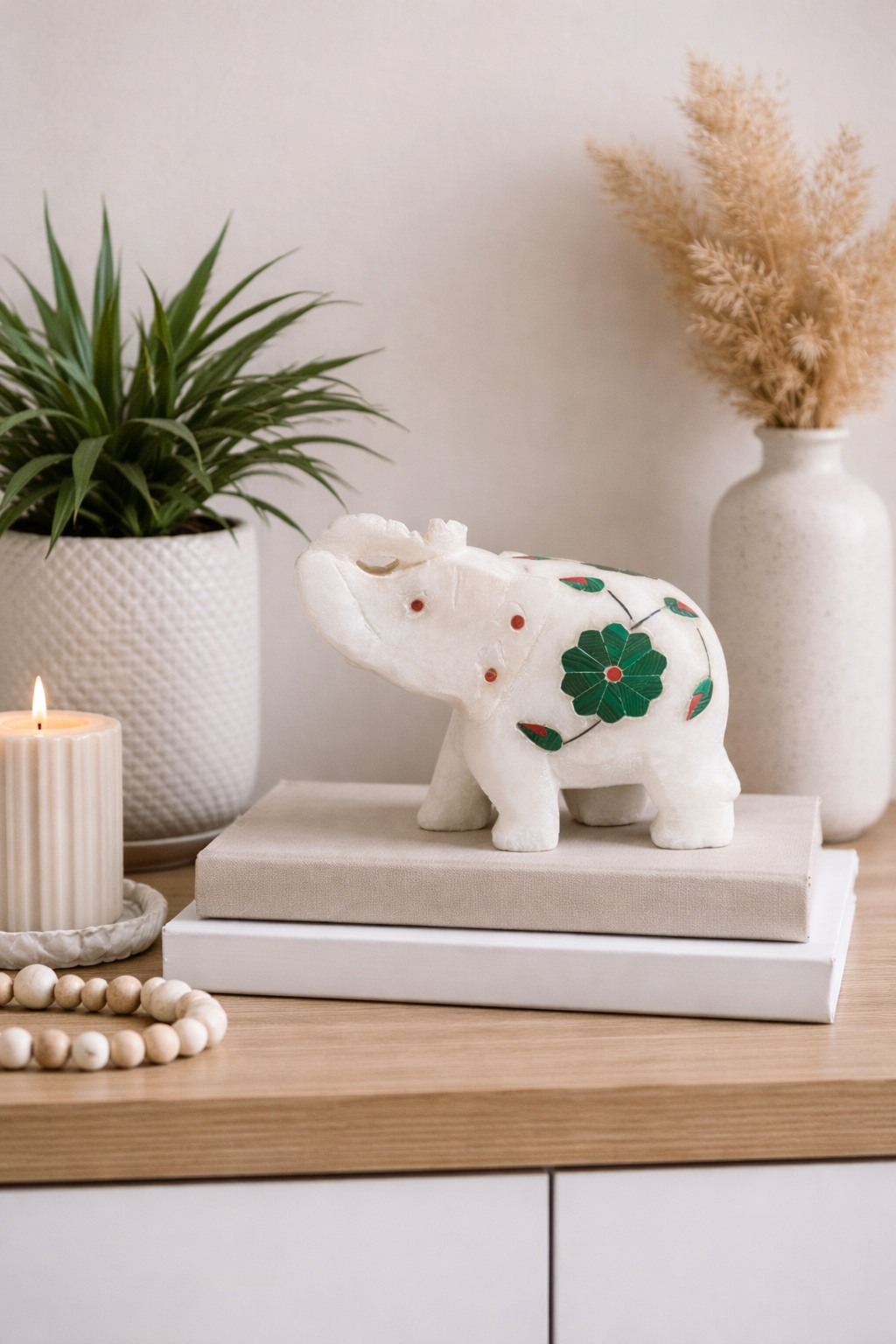 Decorative marble elephant sculpture placed on books with candle and plant, luxury home decor accent