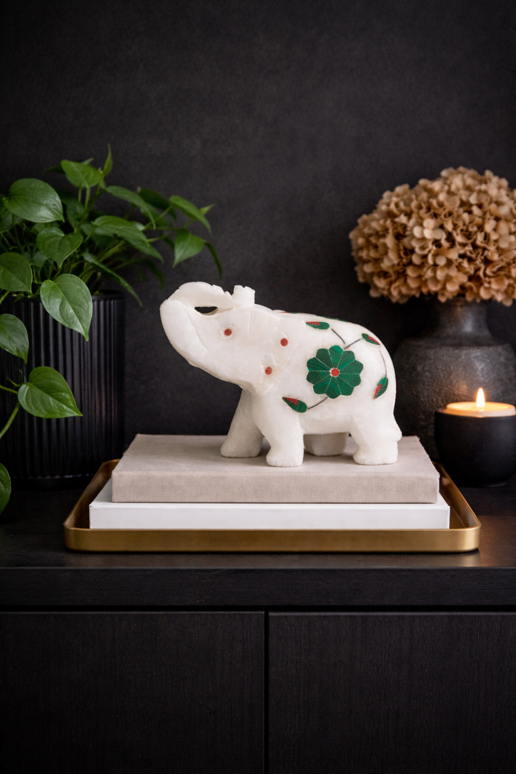 Luxury white marble elephant figurine with green floral inlay displayed on dark console table with candle and plant decor