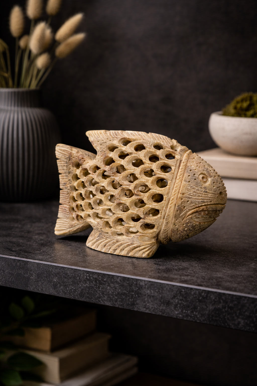 Decorative hand-carved soapstone fish sculpture with hollow lattice detailing, styled on a dark stone console table with a blurred black background