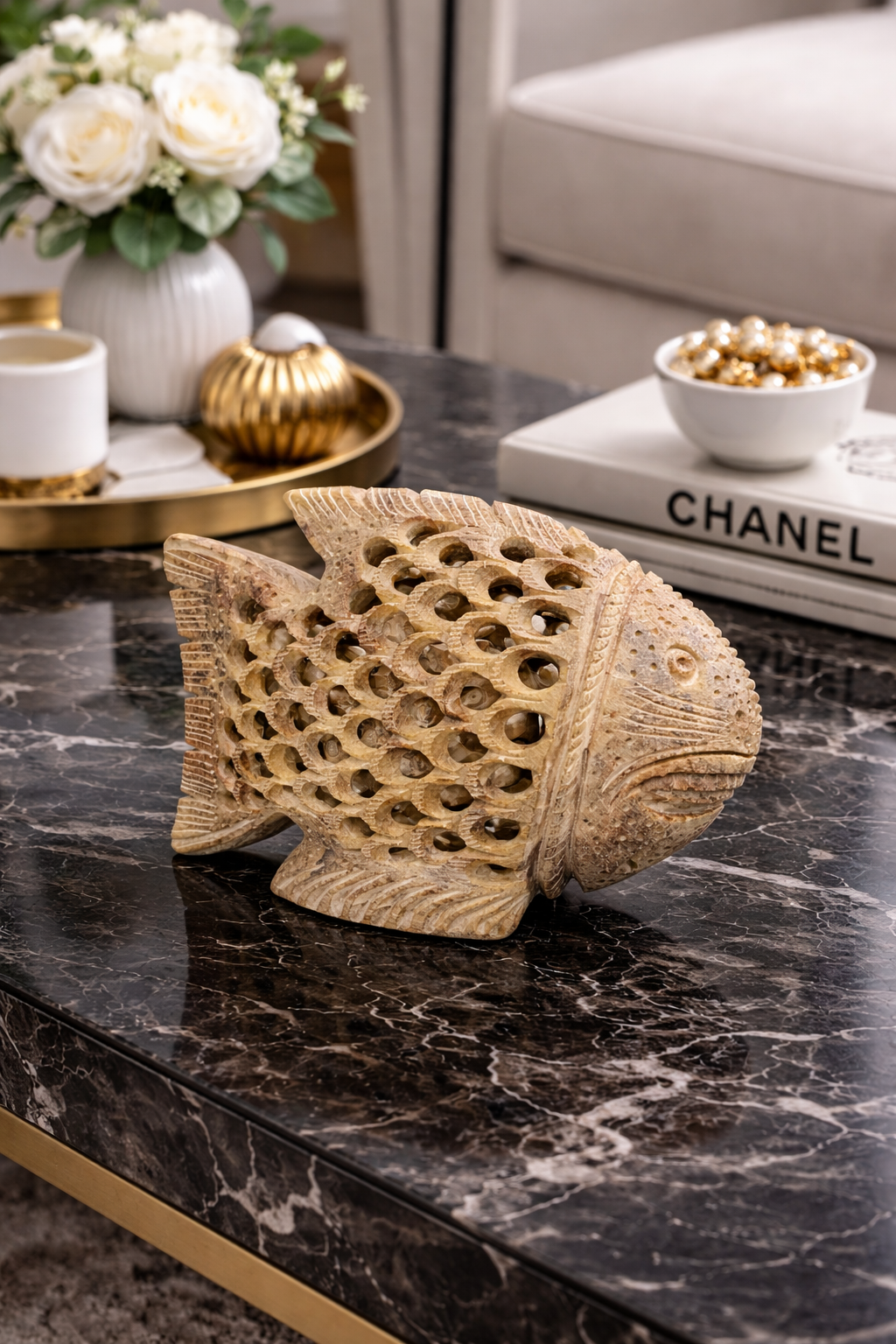 Hand-carved soapstone fish sculpture on black marble coffee table, luxury natural stone home décor styled with flowers and decorative books, modern living room accent.