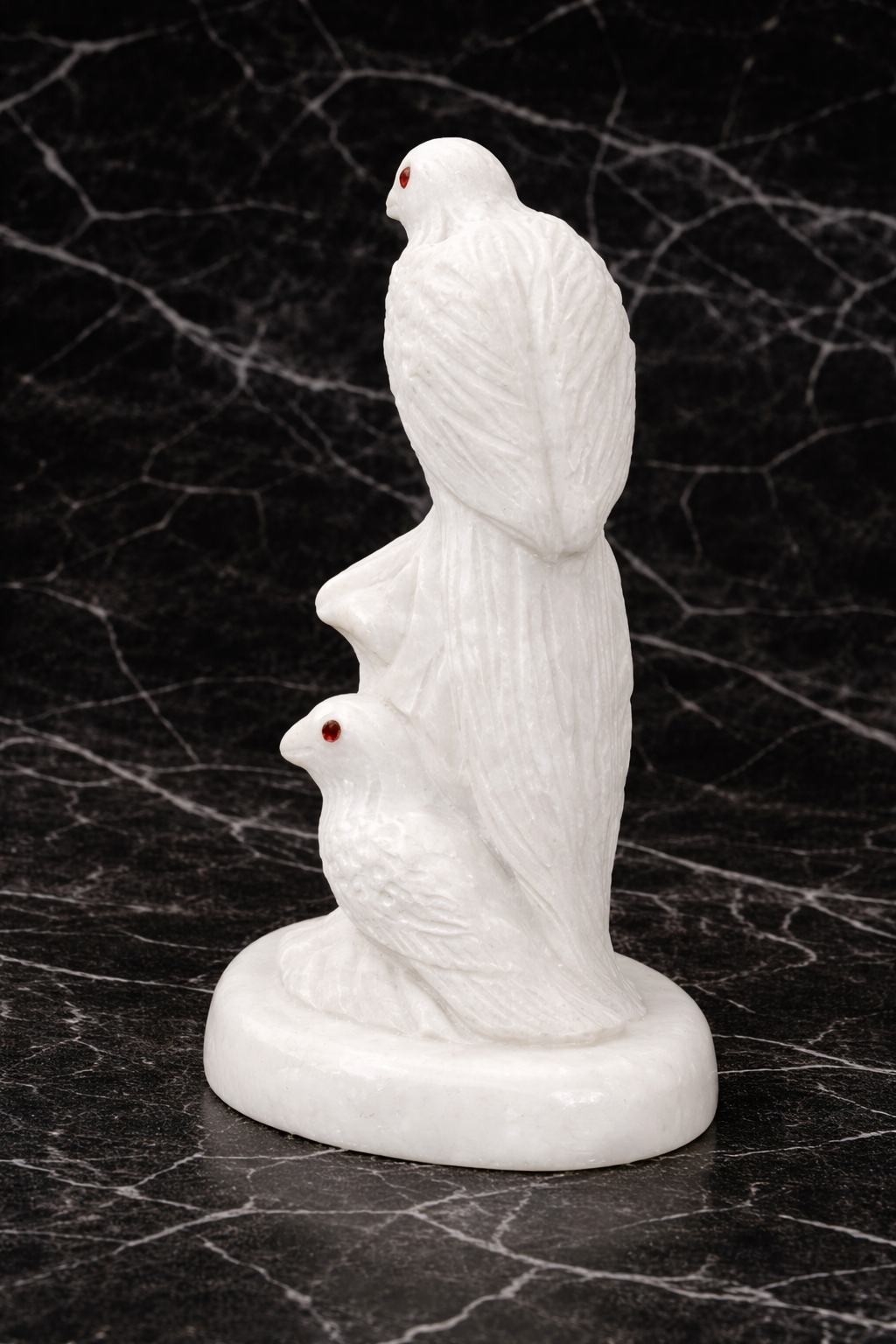 Hand-carved white marble bird sculpture (rear view) with red gemstone eyes on black marble surface