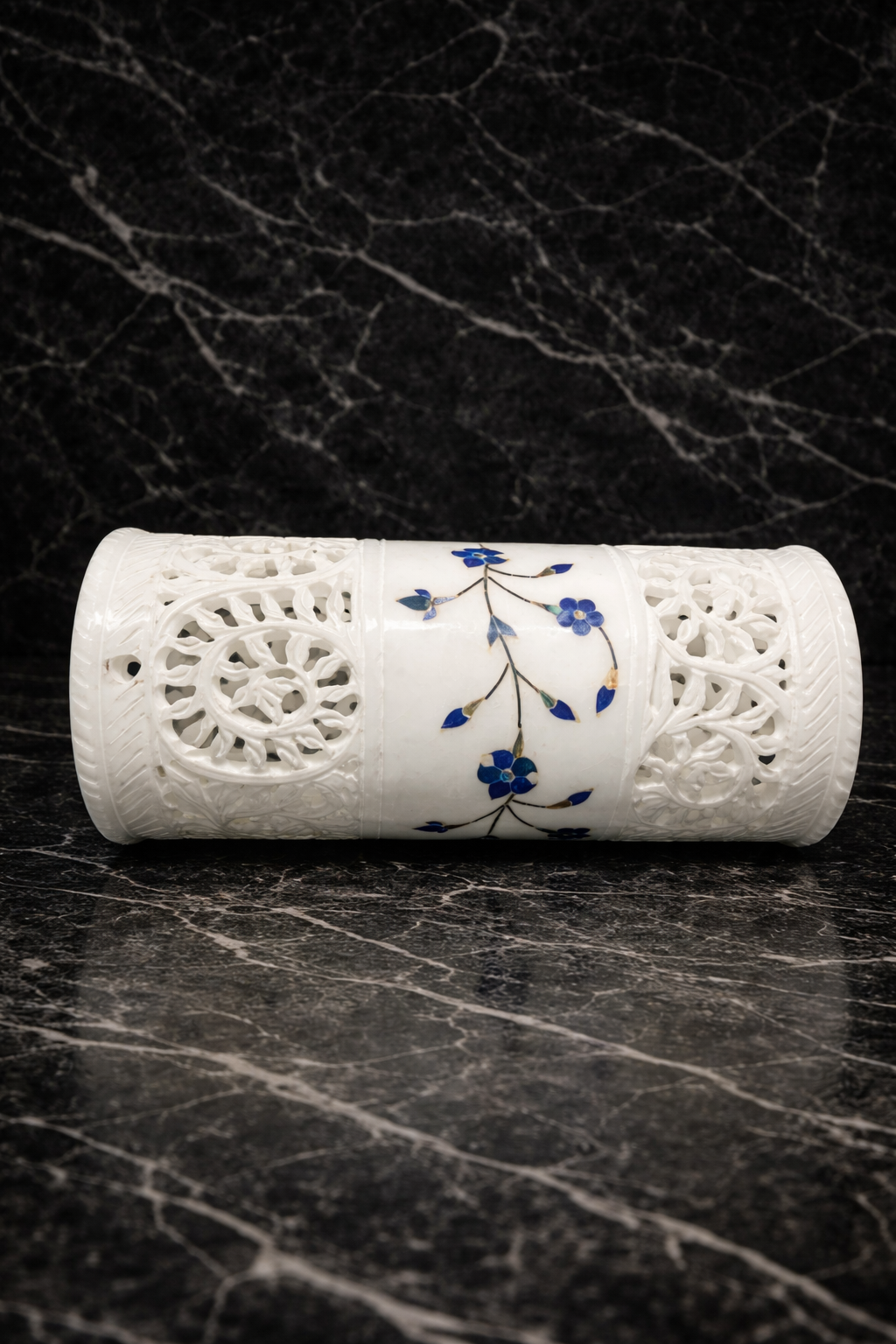 Hand-carved white marble tealight holder with blue floral inlay lying on a black marble surface, luxury artisan marble home décor.