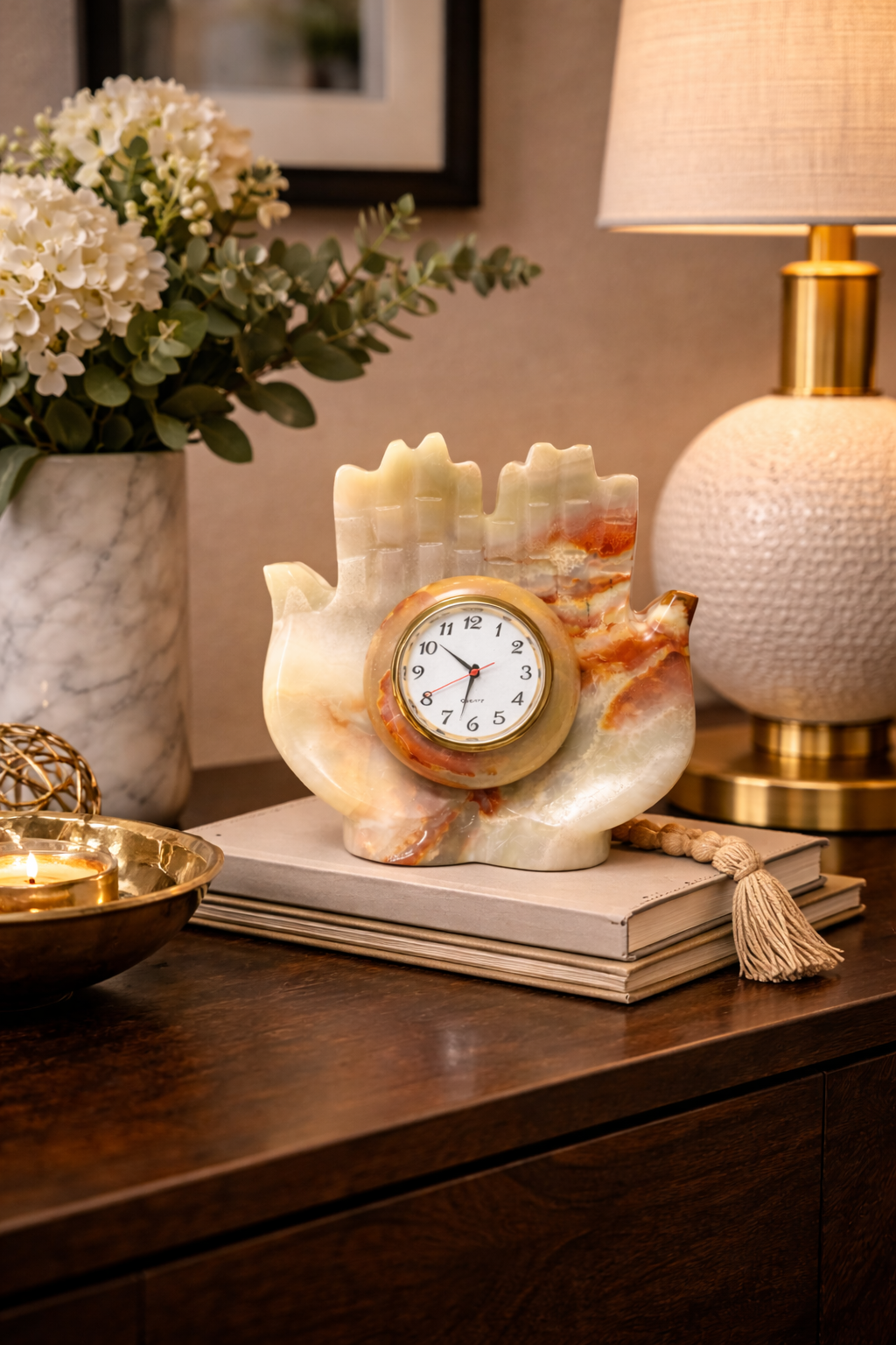 Hand carved natural onyx hand shaped table clock styled on bedside table with lamp flowers and books luxury stone décor