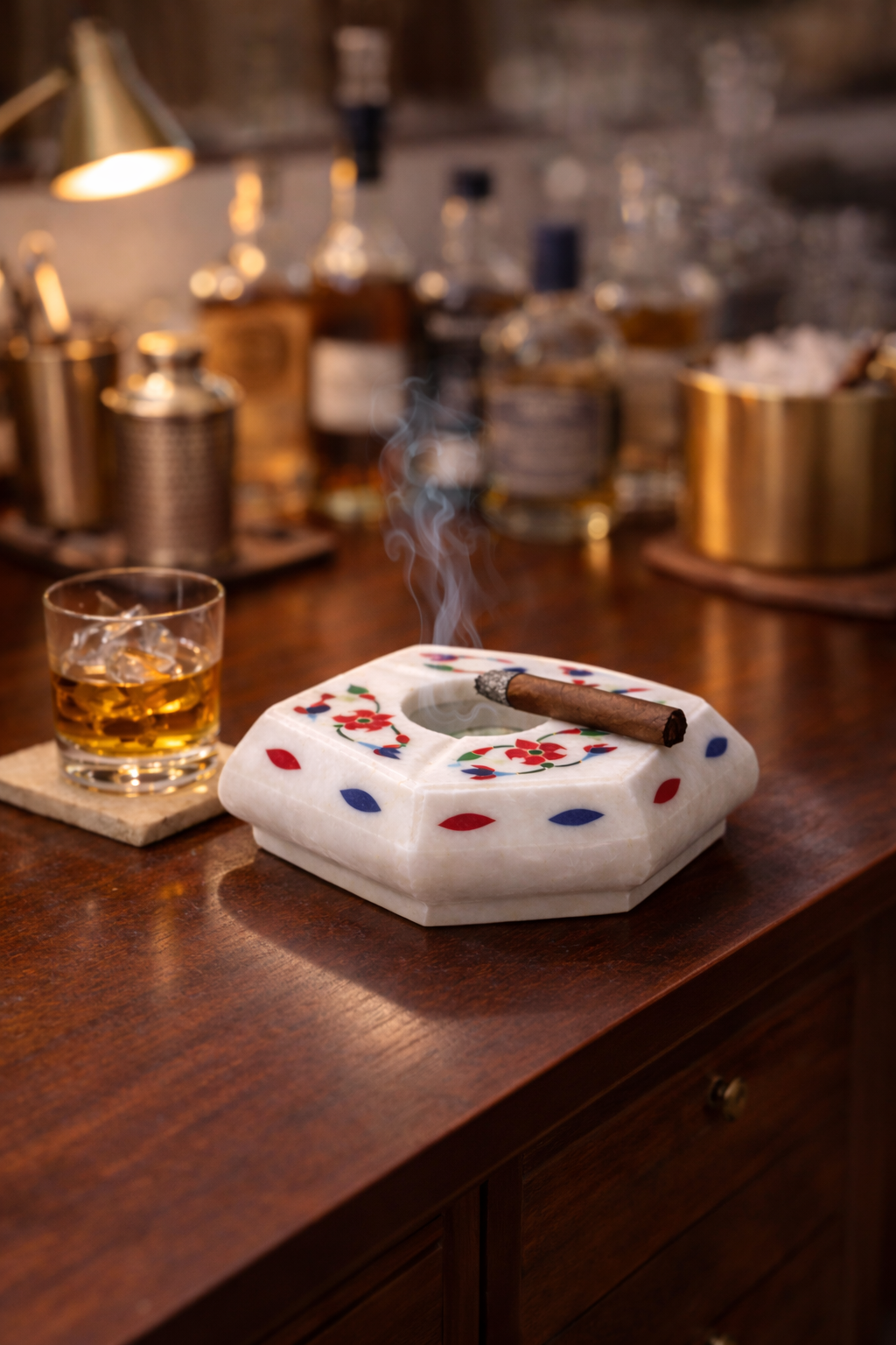 Handcrafted white marble cigar ashtray with colourful floral inlay on luxury home bar table beside whiskey glass