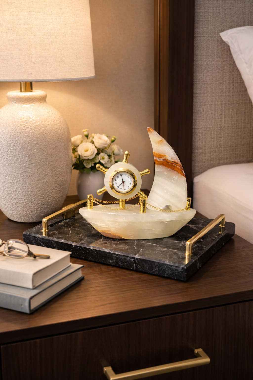Natural onyx ship clock styled on bedside table with lamp and flowers, luxury bedroom decor accent