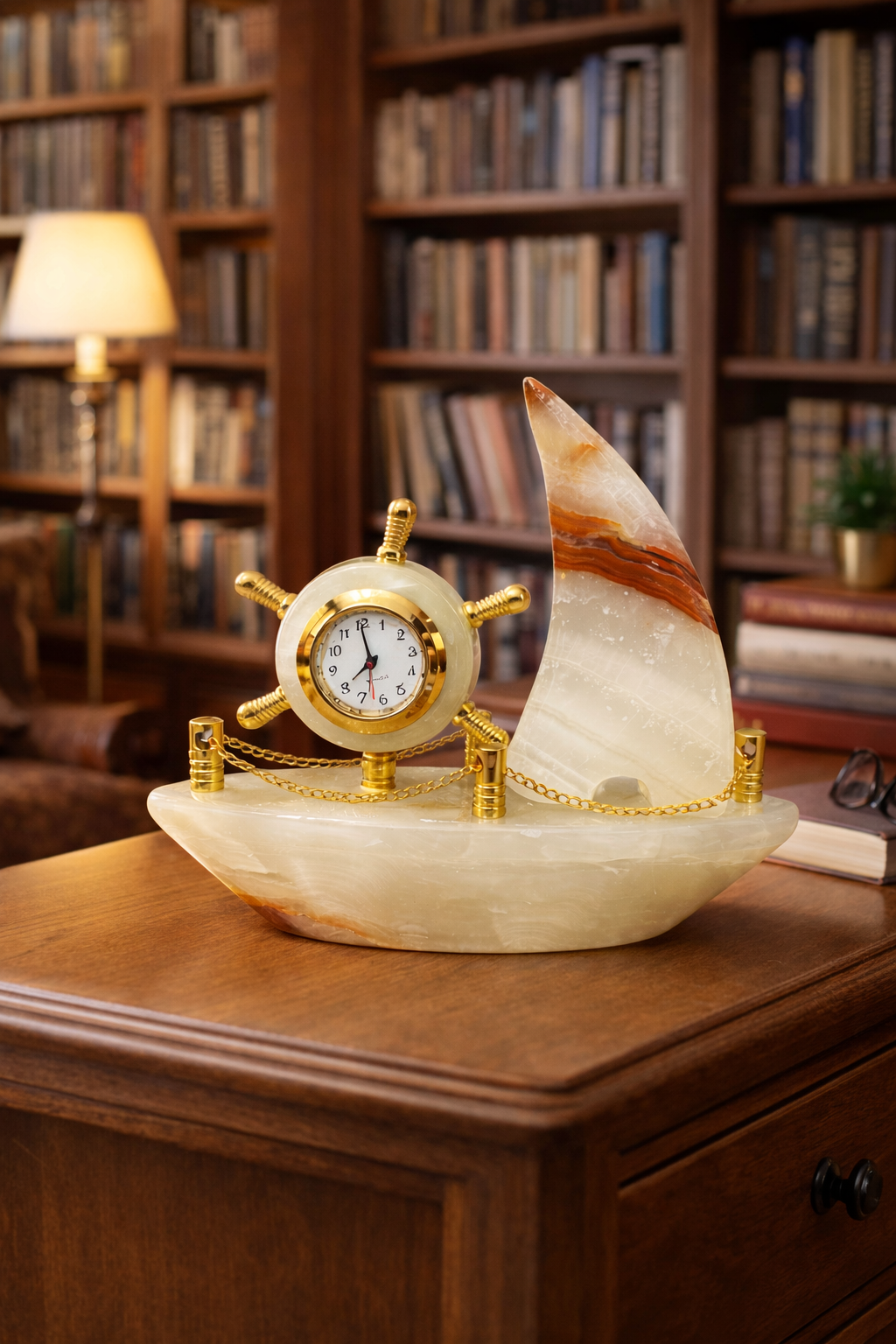 Elegant onyx sailboat clock décor on wooden desk in home library with bookshelves – luxury marble nautical desk decoration.