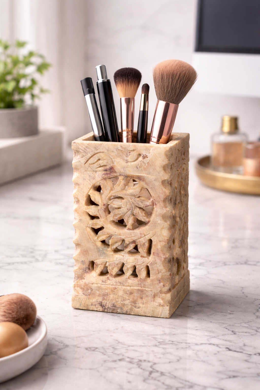 Hand-carved soapstone holder with floral cut-out design used as a makeup brush organiser on a vanity table.