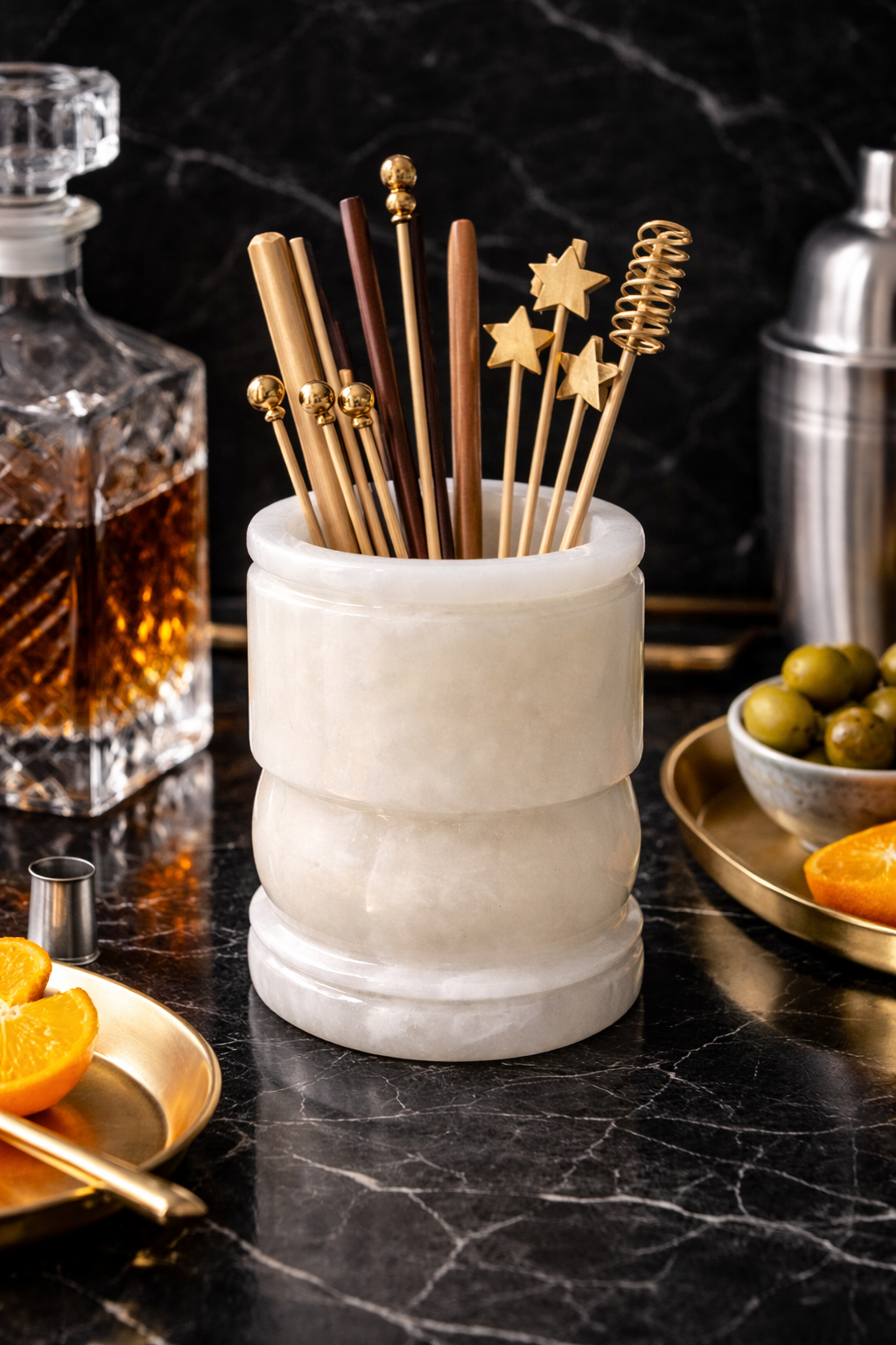 Onyx holder with gold cocktail stirrers on a bar counter with drinks and garnishes.