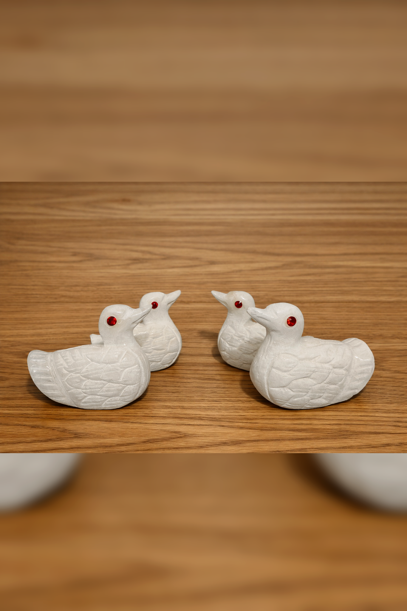 White marble duck figurines with red stone eyes displayed on wooden surface